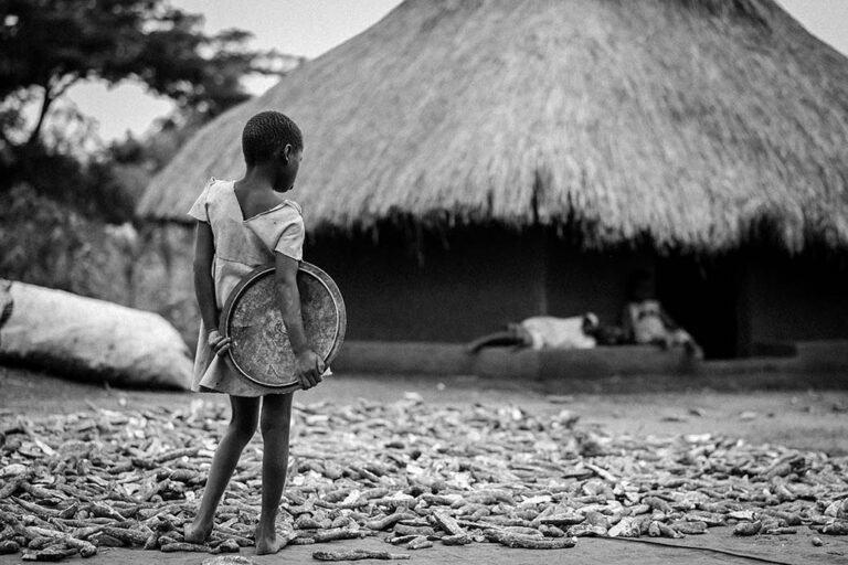 A-young-girl-stands-next-to-cassave-tubers-hung-out-to-dry-at-a-homestead-photographer-in-kenya